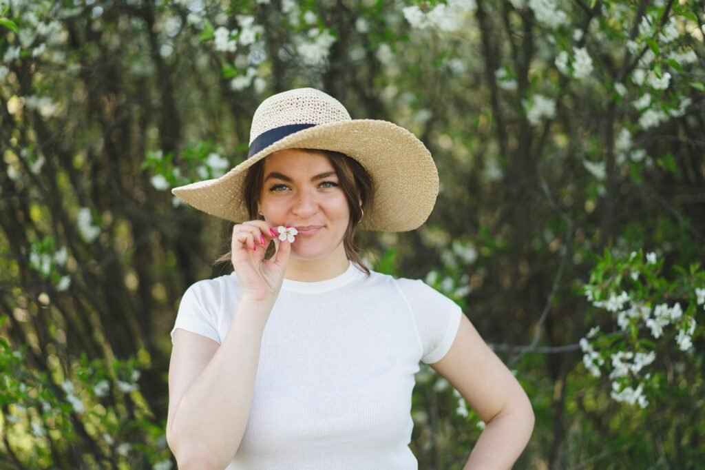 Young funny beautiful woman in a hat among flowering trees. Breathe free. Happy woman no allergy
